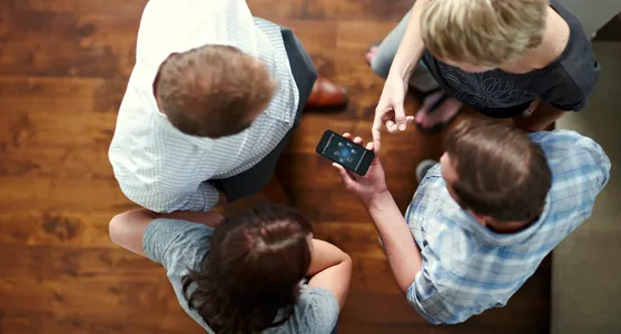 A group of people sitting on the floor looking at a phone.