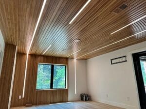 Empty room interior during construction with wood paneled walls and ceiling and integrated linear LED lights.