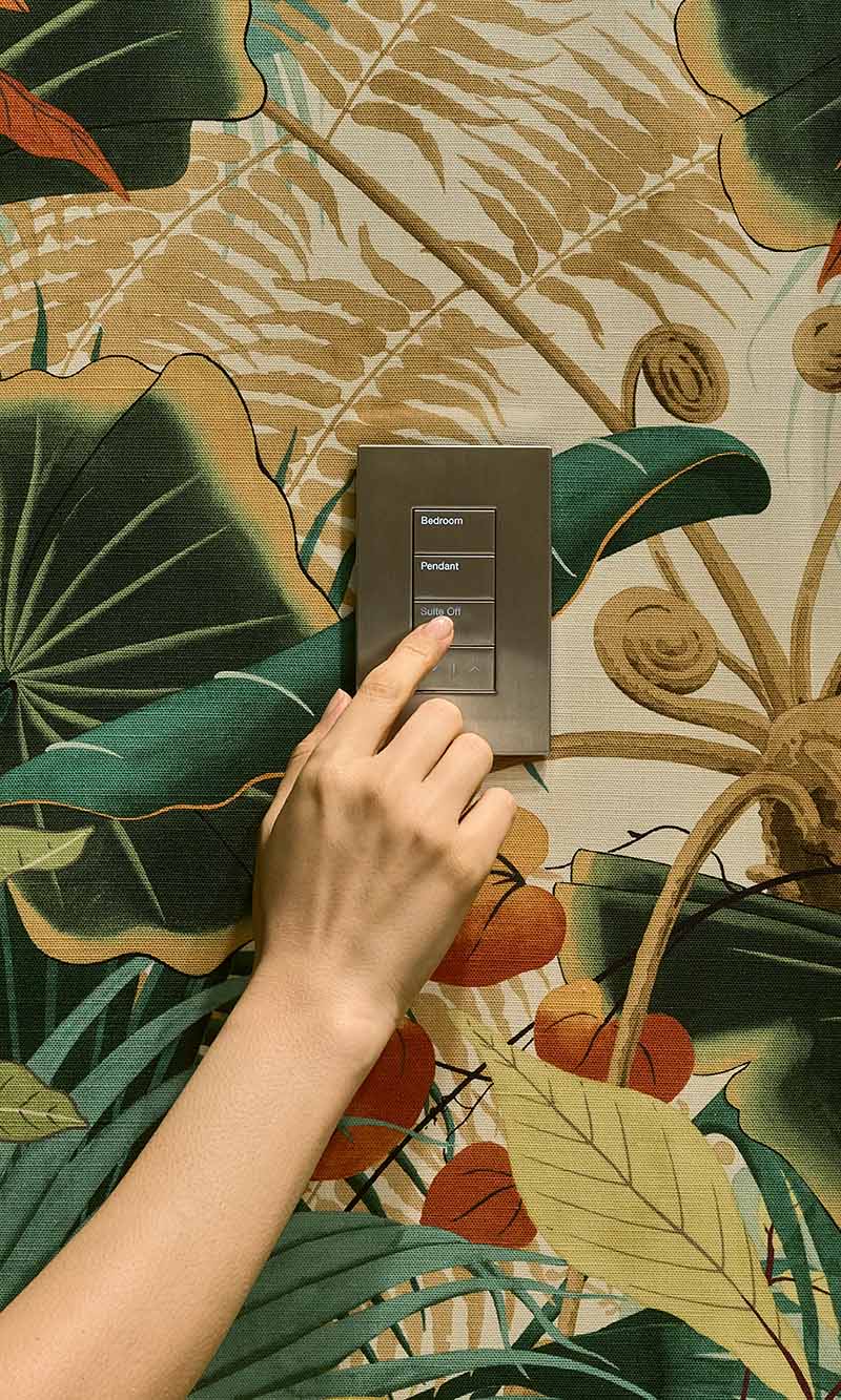 A sleek black electronic keypad interface mounted on a textured brick wall with green ivy vines growing around it.