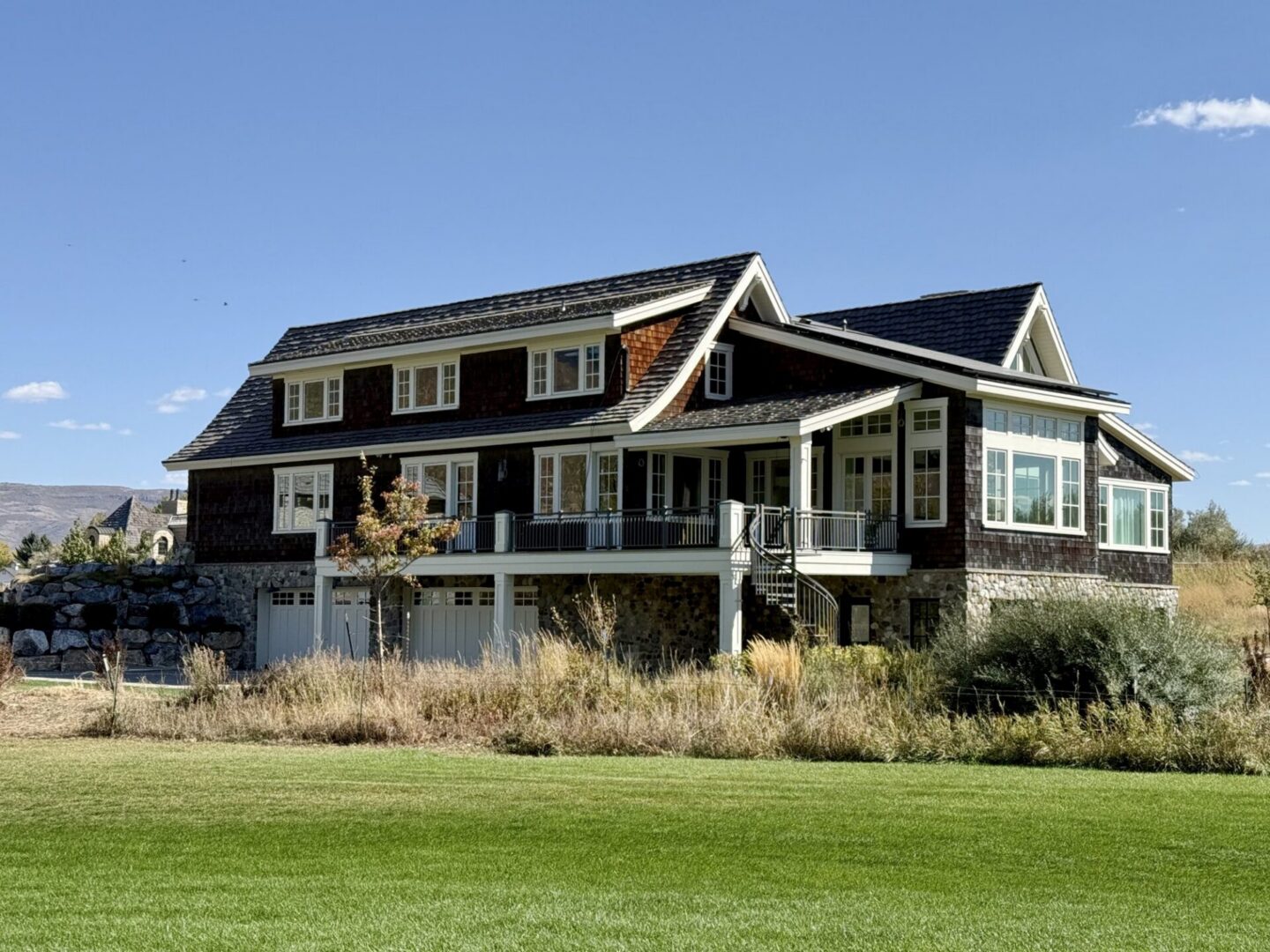Exterior of a shingle-style custom smart home with stone accents and wraparound deck in Colorado